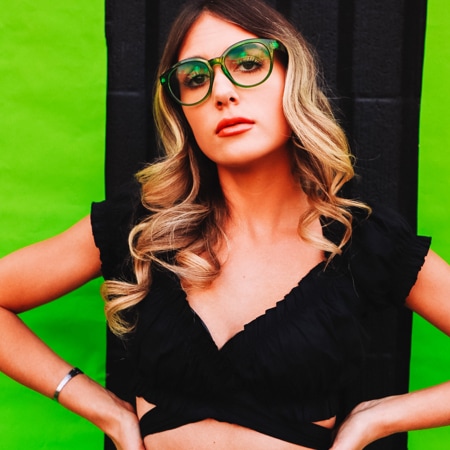 Kalianna Carpenter wearing Zenni round glasses #206024 in front of a black and green background.