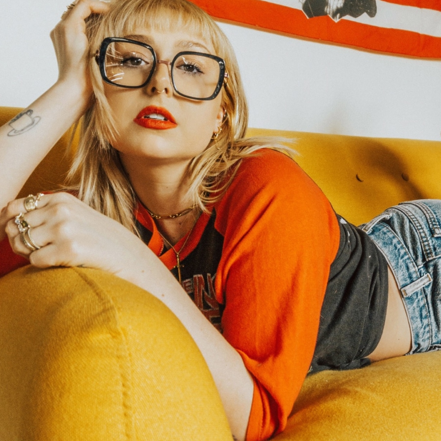 Image of a woman wearing square-shaped glasses, lying on a yellow couch.