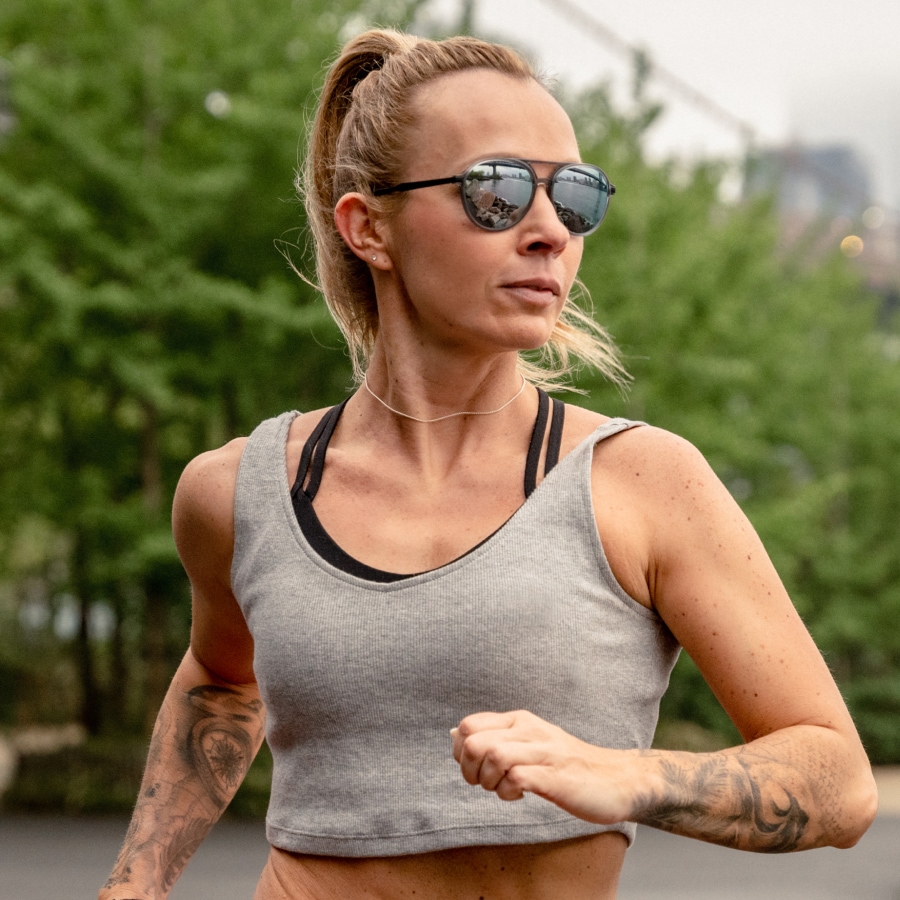 Image of a woman jogging, wearing workout gear and a pair of aviator sunglasses on a runner’s path.