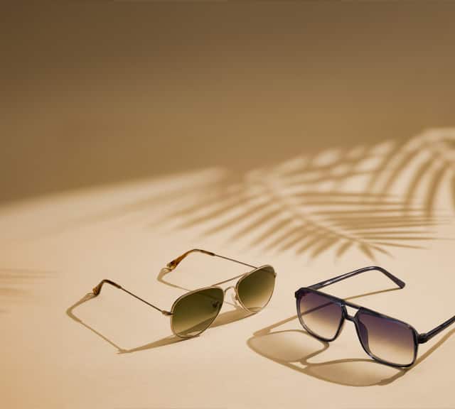 2 pairs of aviator sunglasses with palm tree shadow on a light brown background.