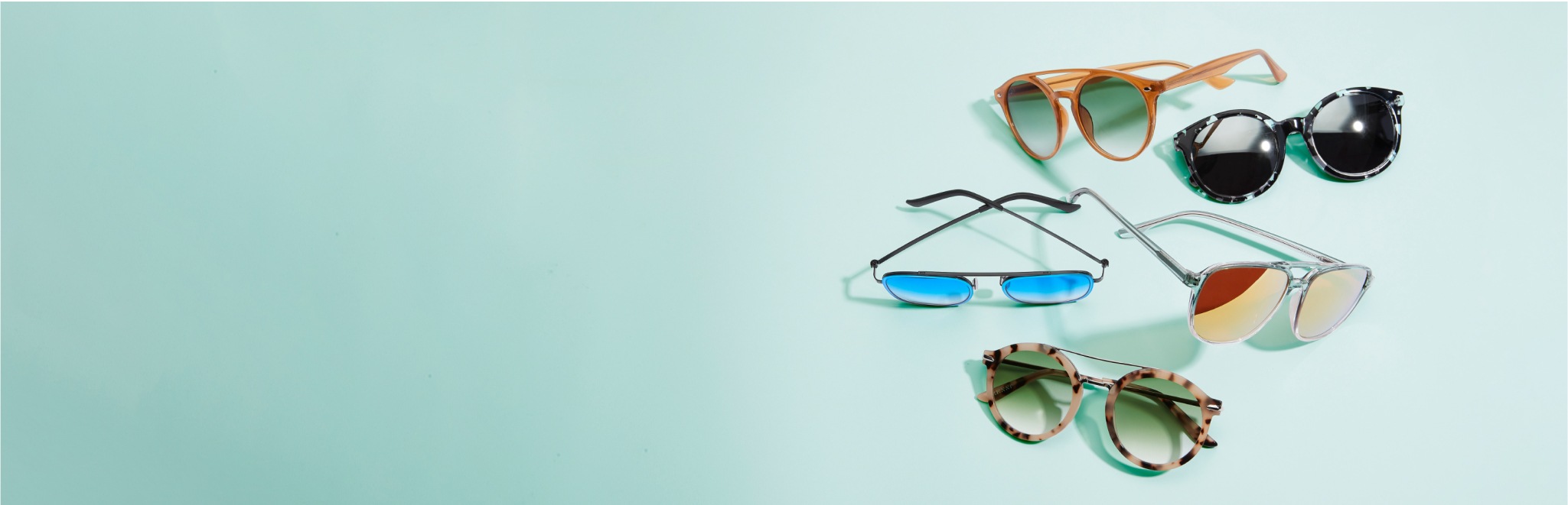 Teal background with 5 sunglasses: brown with ombre lenses, black tortoiseshell with dark grey lenses, black aviators with blue mirror lenses, transparent aviators with gold mirror lenses, and tortoiseshell with ombre lenses.