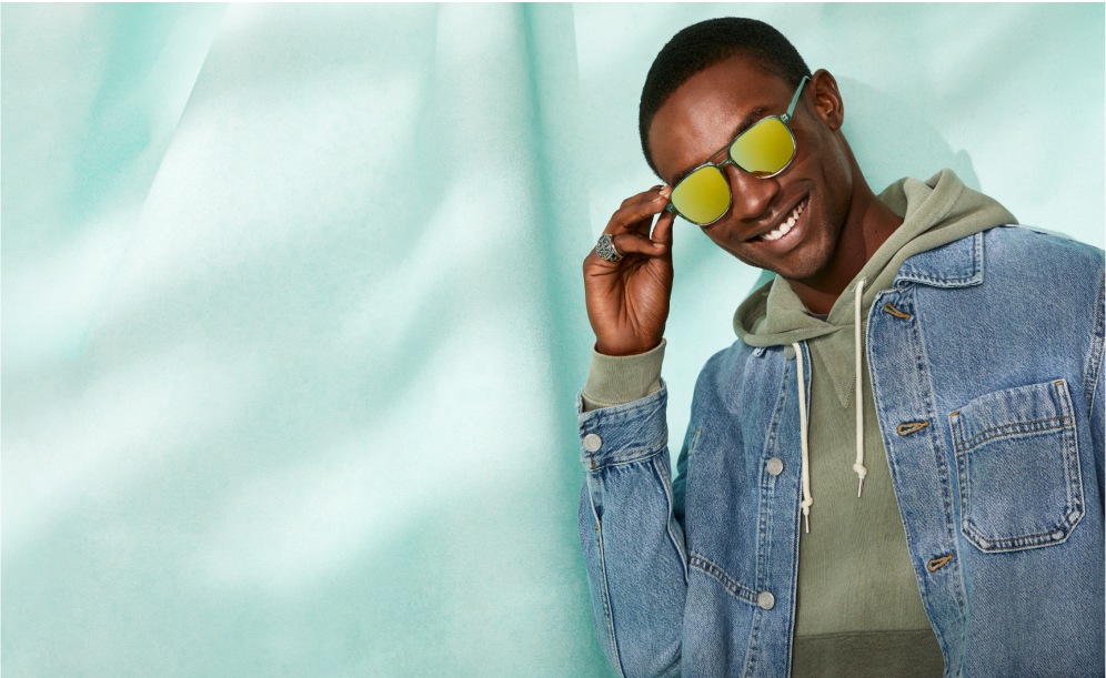 A man model wearing Zenni sunglasses with gold mirror lens coating in front of a teal background.