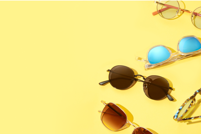A variety of stylish sunglasses, including round metal frames and clear frames with mirrored lenses, on a yellow background.