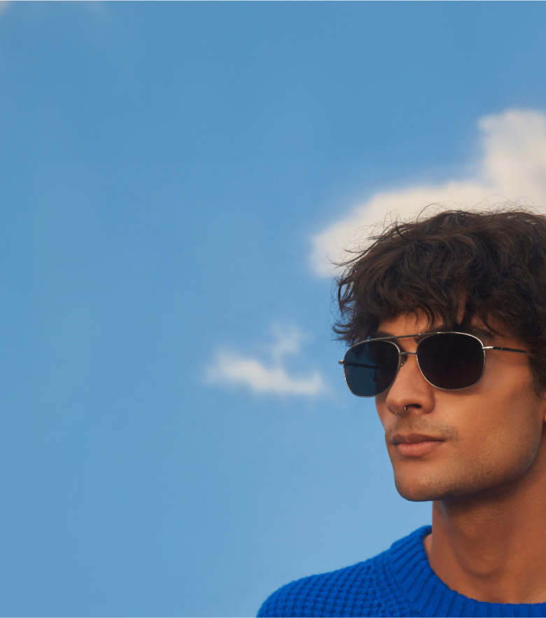 A man in a bright blue sweater and metal aviator sunglasses with dark lenses.