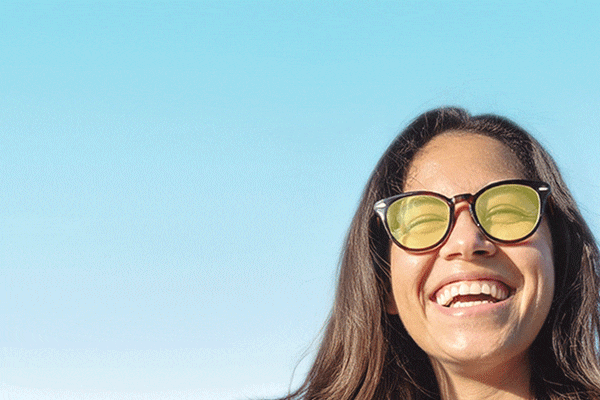 Woman with long hair and big smile wearing Zenni round glasses with sunglasses tint different colors.