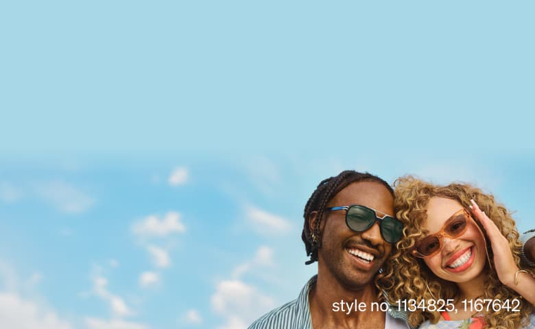 Two smiling people wearing stylish sunglasses—one in dark green rectangular frames and the other in oversized translucent pink frames—posing closely under a bright blue sky with soft clouds, exuding a cheerful summer vibe. Style no. 1134825, 1167642.