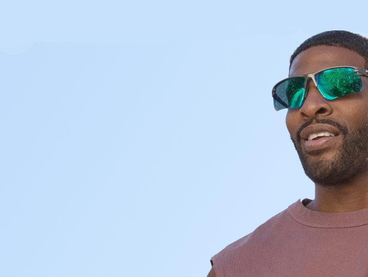 A man with short curly black hair and a short beard wearing silver half-rim sports sunglasses with green mirror lenses.
