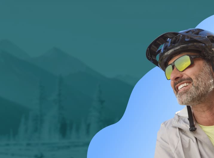 A man with a salt and pepper beard wearing a bike helmet and black sports sunglasses with yellow mirror lenses.