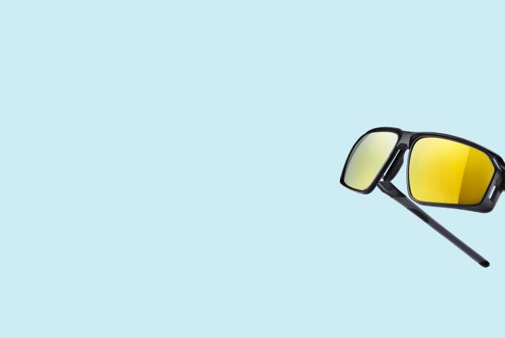 Black sports sunglasses with lens vents and yellow mirror lenses. Light blue background.