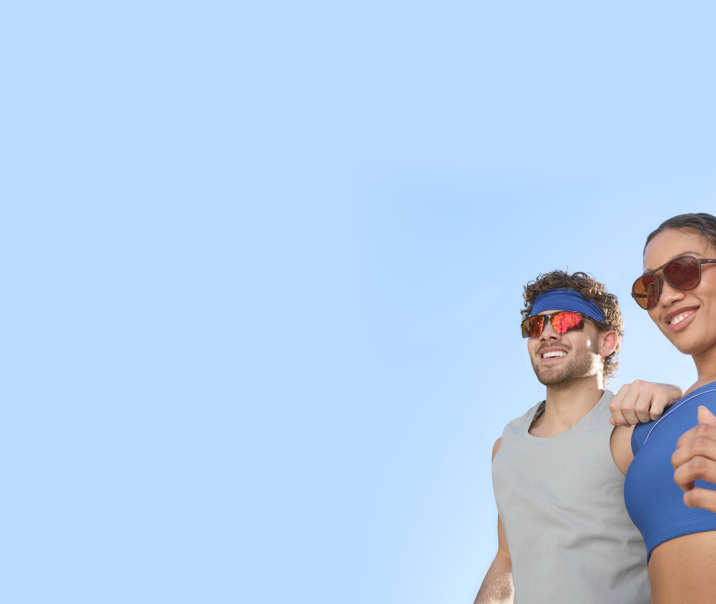 A man and a woman jogging. He’s wearing silver half-rim sports sunglasses with red mirror lenses. She’s wearing tortoiseshell aviator sports sunglasses with dark brown lenses.