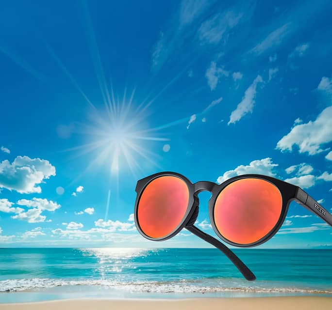 Matte black round sunglasses with vibrant red mirrored lenses floating over a sunny beach and ocean background under a white "Zunscreen" logo.