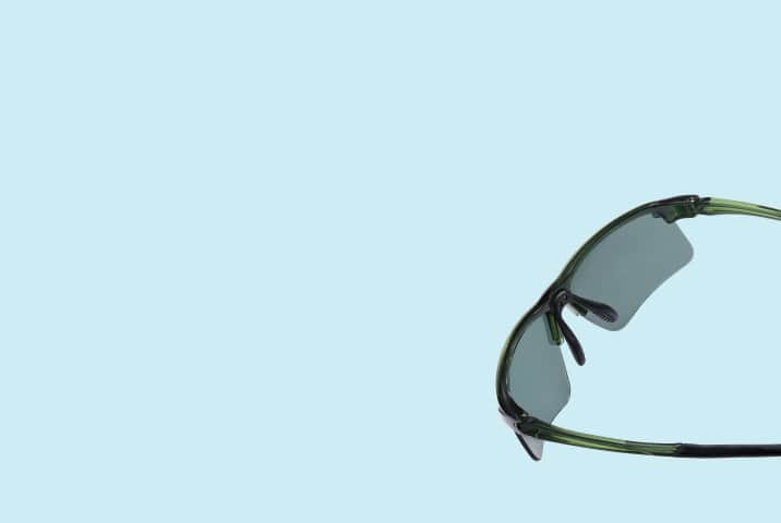 Close-up of semi-rimless sport sunglasses with translucent green frames and dark grey lenses, floating against a solid light blue background.