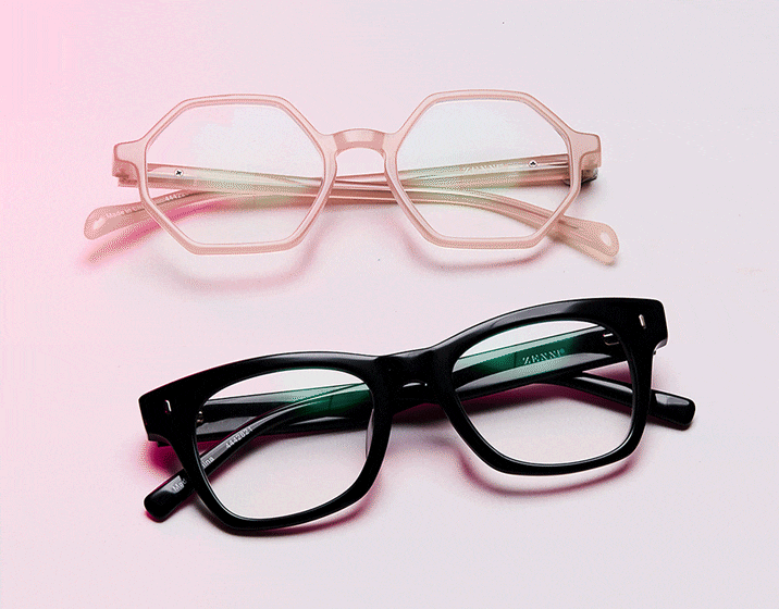 Pink geometric glasses and black square glasses with Transitions GEN S lenses that change from clear to dark. Peach and pink background.