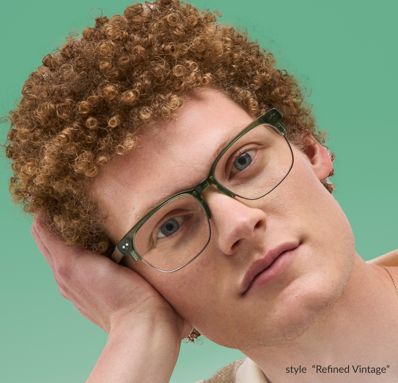 A man with curly hair wearing green browline style “Refined Vintage” Timo x Zenni glasses against a light green background, resting his head on his hand.