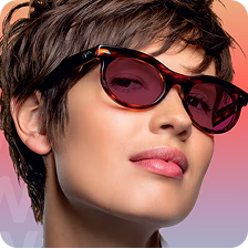 A woman in tortoiseshell glasses with ruby red Transitions Gen S lenses that change from clear to dark.