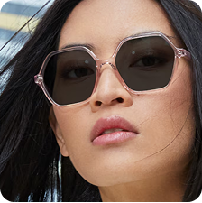 An Asian woman with long black hair wearing clear geometric frame glasses with Transitions lenses that turn from clear to dark.