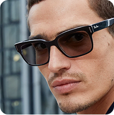 A man with short brown hair wearing black rectangular frames with Transitions lenses that turn from clear to dark.