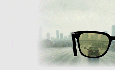 Animated image showing the light-responsive tints of Transitions Drivewear sunglasses lenses. Slide one shows a pair of black sunglasses superimposed over a highway on a sunny day, with dark brown lenses. Slide two shows the highway in the evening and the lenses are now copper. Slide three shows the highway on a cloudy day and the lenses are now olive green.