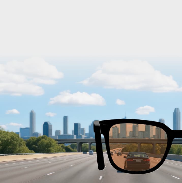 Image showing the light-responsive tints of Transitions Drivewear sunglasses lenses with black sunglasses superimposed over a highway on a sunny day, with dark brown lenses. 