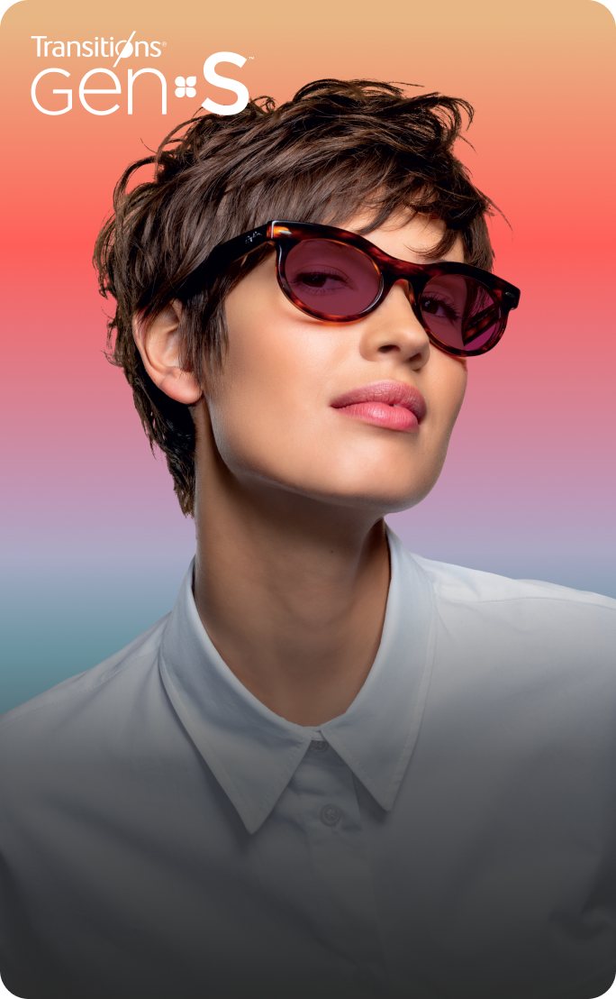 A woman in tortoiseshell glasses with ruby red Transitions Gen S lenses that change from clear to dark.