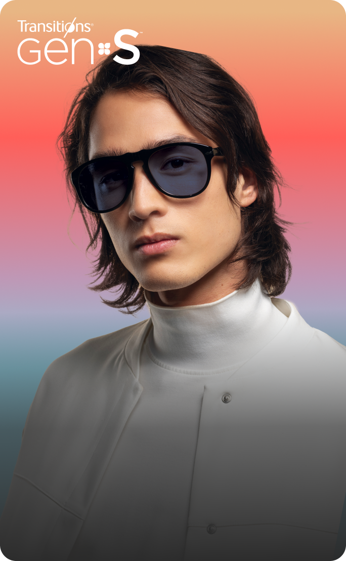 A young man with shoulder-length dark hair wears large black sunglasses with a Transitions GEN S lens in dark gray.