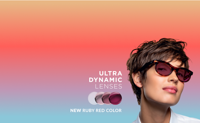 A woman in tortoiseshell glasses with ruby red Transitions Gen S lenses that change from clear to dark.