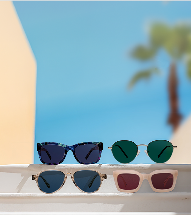 Four pairs of sunglasses with Transitions® lens on white steps with a clear blue sky and a palm tree in the background.