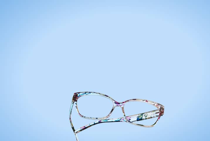 Lunettes rectangulaires avec une monture à motif floral coloré inclinées sur fond bleu clair.