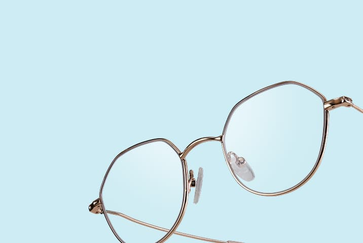 Gros plan sur de fines lunettes géométriques en métal or rose inclinées sur fond bleu clair.