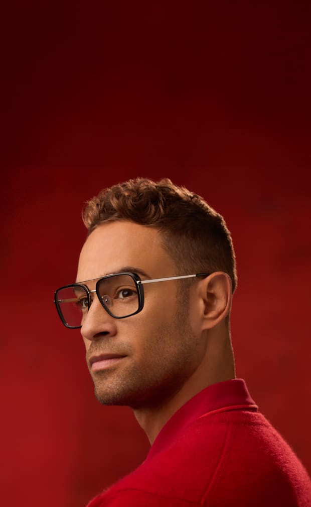 Male model in oversized square aviator-style Zenni glasses with black rims and gold metal accents, set against a red backdrop.