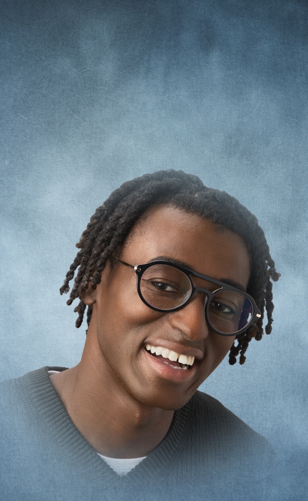 Young man wearing Zenni black aviator frames and a dark sweater against a gray textured background.
