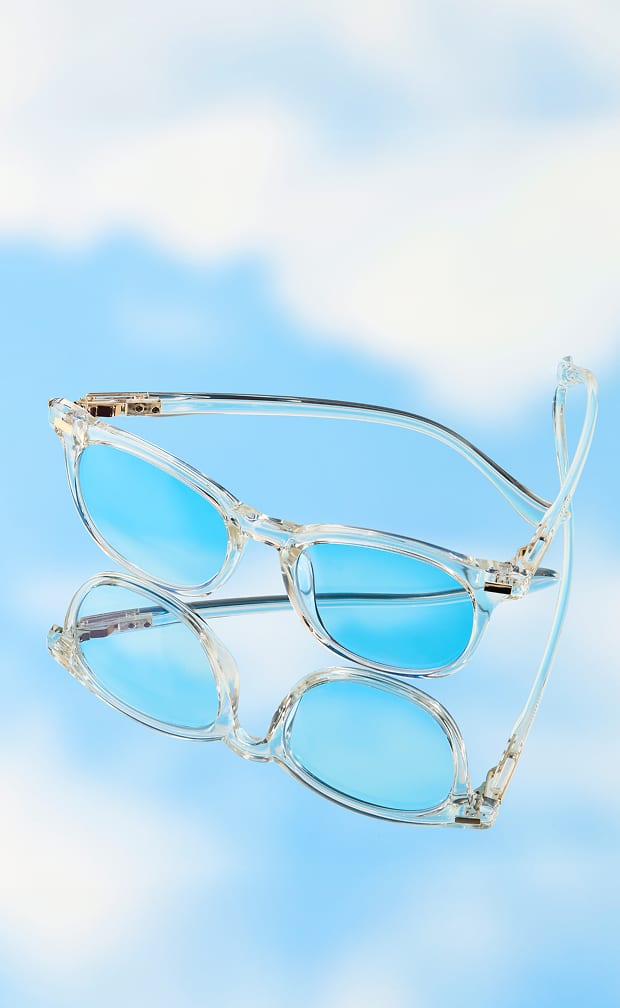 A pair of clear rectangular glasses with blue-tinted lenses resting on a reflective surface that mirrors a blue sky with white clouds.