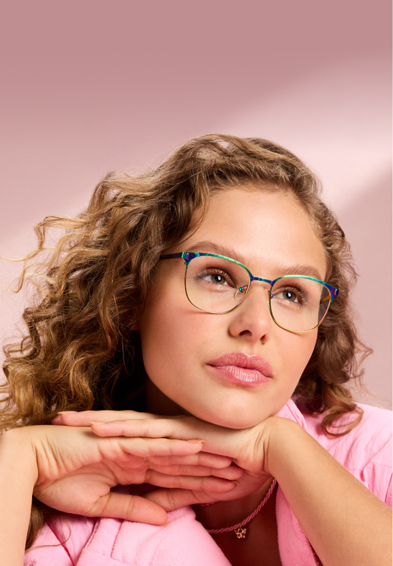 A woman with blond curly hair wearing rainbow metal square Zenni glasses, on a pink background.