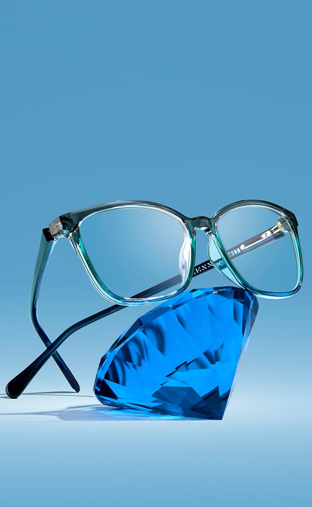 A pair of translucent teal glasses balanced on top of a large, multifaceted blue gemstone against a solid blue background.