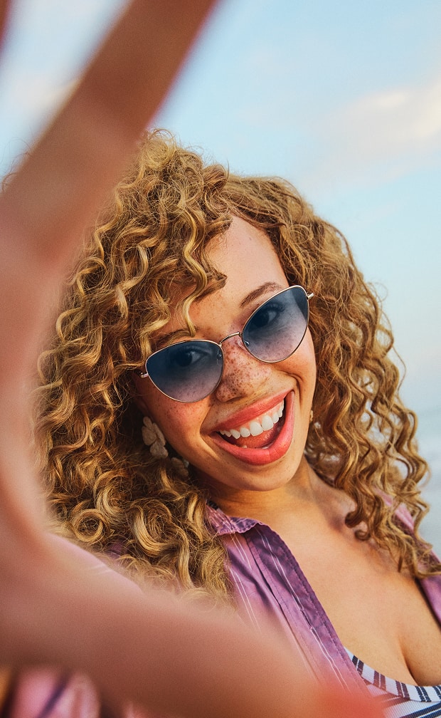 Woman in Zenni blue gradient sunglasses smiling with blue sky background.