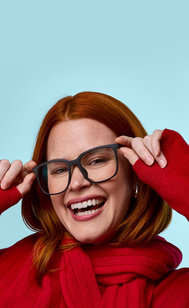 Red-haired woman in Zenni black square glasses with a red sweater against a sky-blue background.