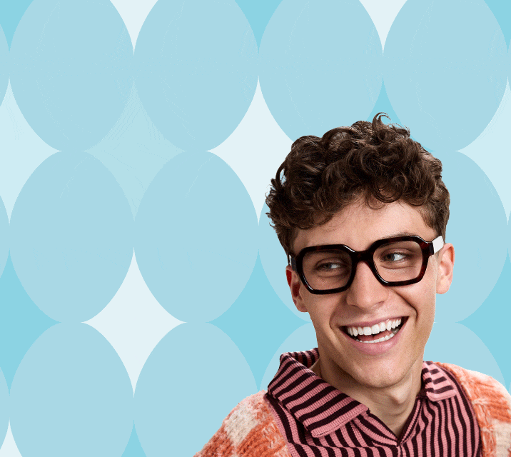 Man smiling wearing trendy dark square glasses pose in front of an blue patterned background.