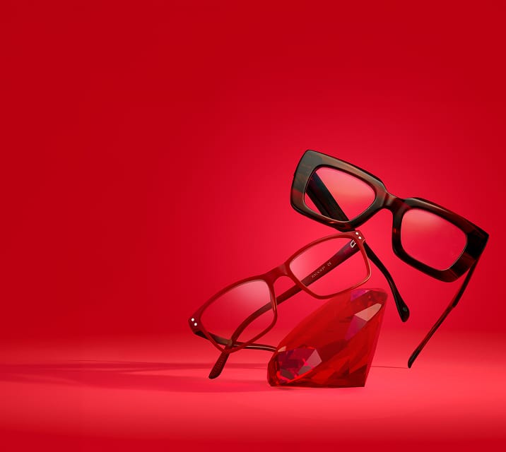Oversized red rectangle glasses and rectangle red glasses resting on a giant red ruby, on a bright red background.