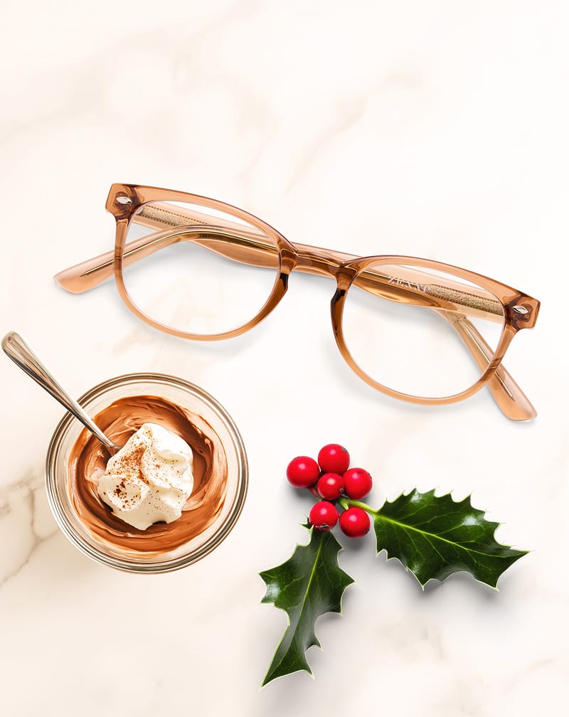 Tan translucent Zenni glasses on a marble surface beside whipped chocolate mousse and red holly berries.