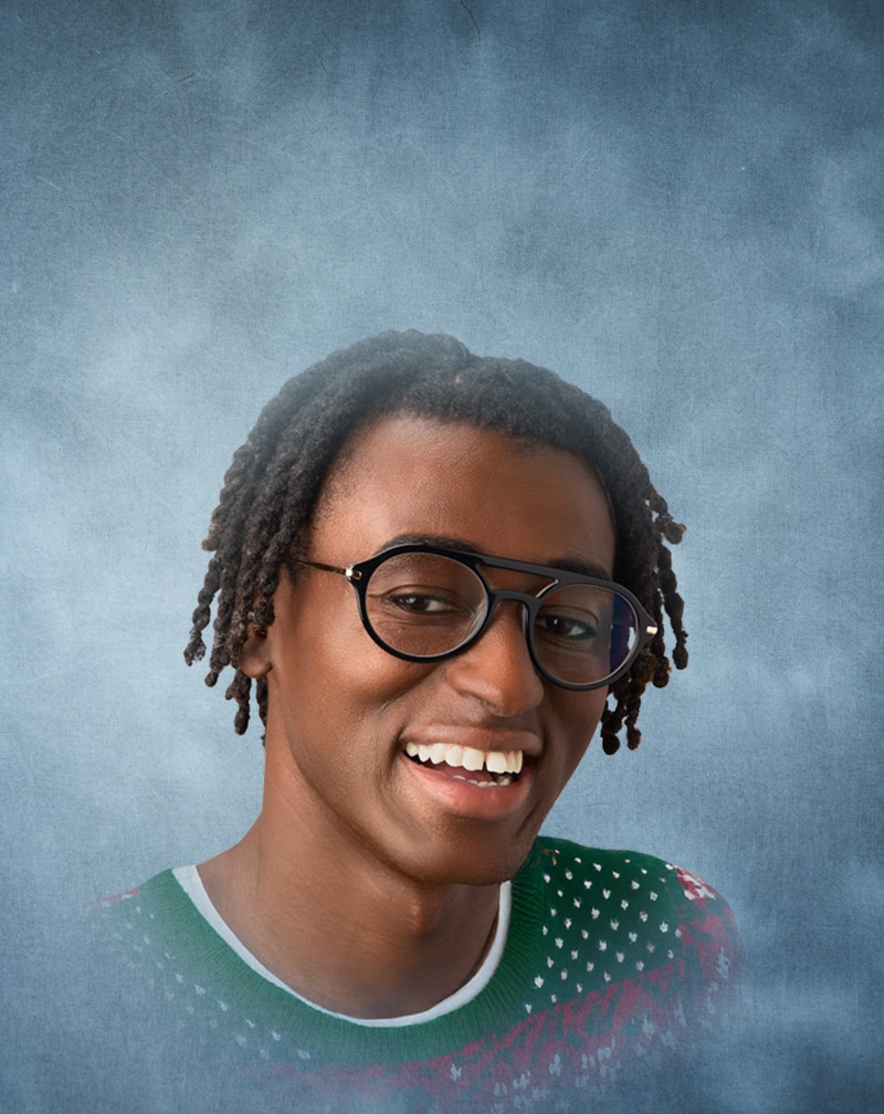 Young man wearing Zenni black aviator frames and a green patterned sweater against a gray textured background.