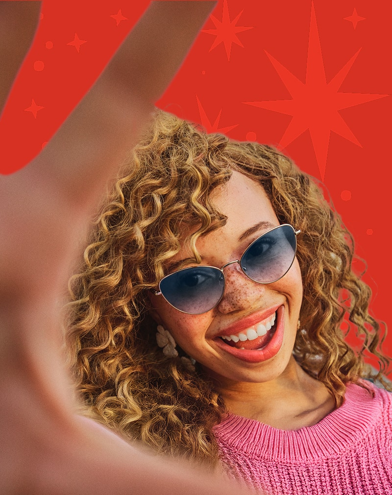 Smiling woman in Zenni dark gradient tint sunglasses with curly hair against a red starburst background.