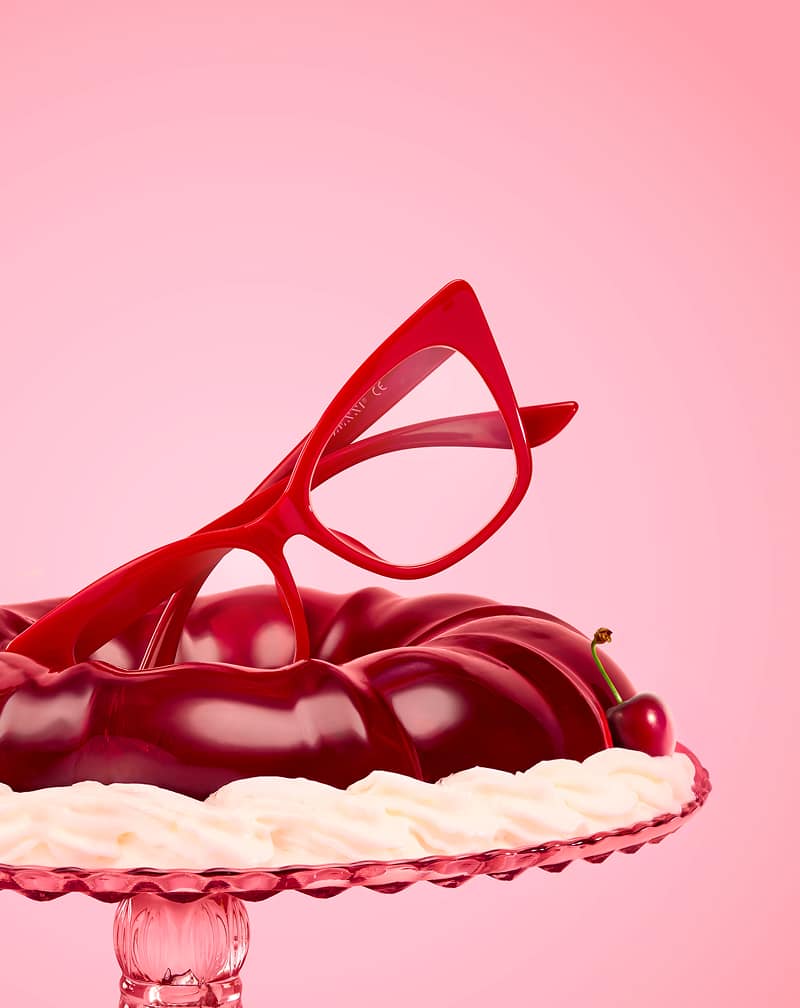 Red glasses resting atop a glossy red gelatin dessert and cherry garnish on a pink background.