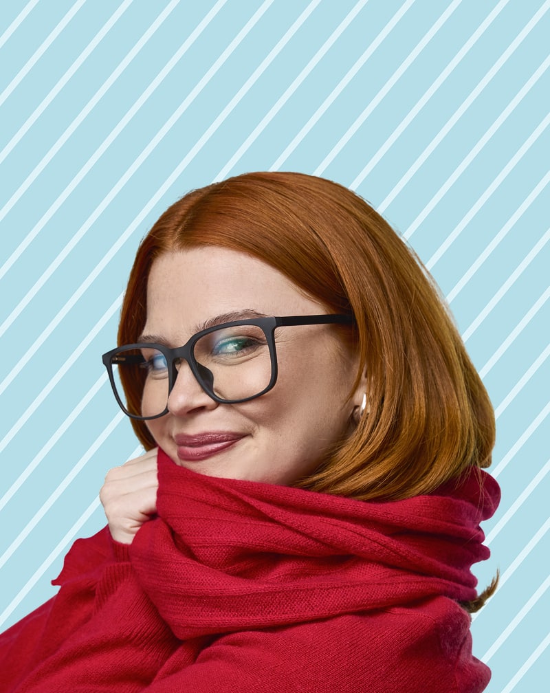 Red-haired woman in Zenni black square glasses with a red sweater against a blue and white striped background.
