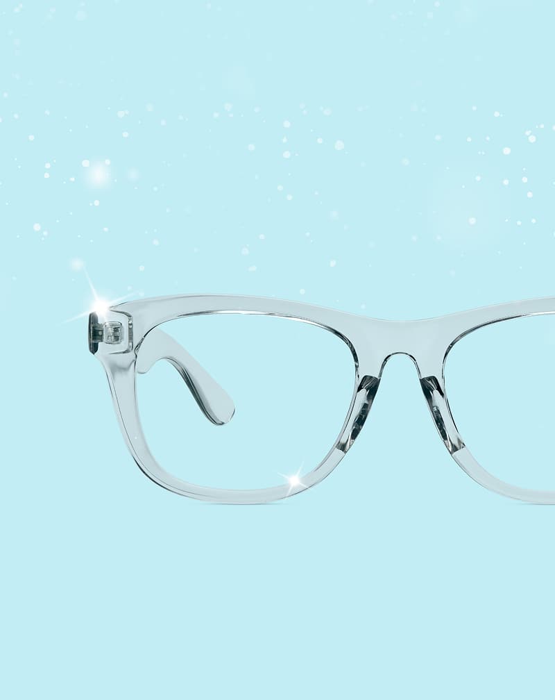 Transparent Zenni eyeglass frames displayed on a light blue background with a sparkling, snowy effect.