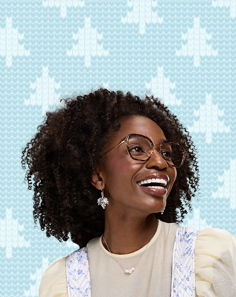 Smiling woman in Zenni cottagecore brown frame glasses with a soft teal needlepoint background.