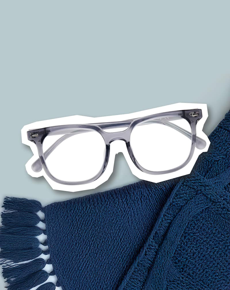 Gray Zenni eyeglasses placed on white cutout over folded blue knit fabrics and gray background.