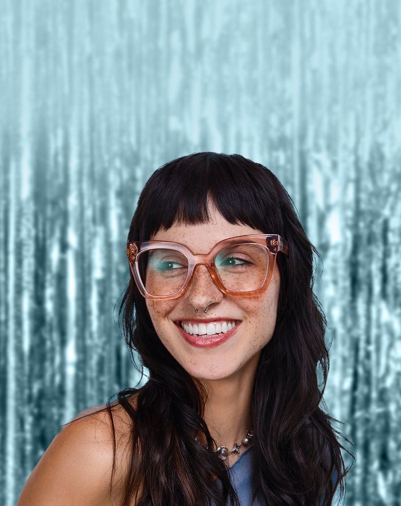 Smiling woman wearing Zenni large brown translucent glasses in front of a silver metallic background.