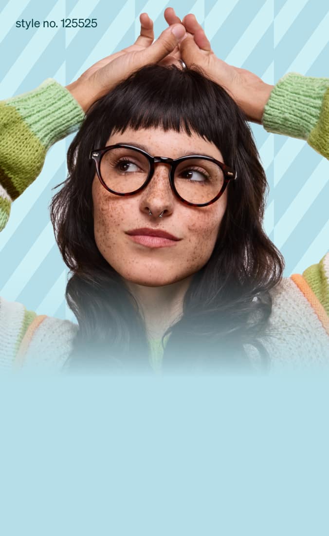 A woman with dark wavy hair and freckles, dressed in a cozy, multicolored striped sweater, wearing round tortoiseshell glasses.