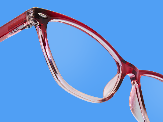 Gros plan sur des lunettes papillon en rouge translucide inclinées sur fond bleu éclatant.