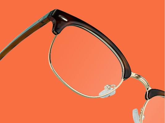 Gros plan sur des lunettes style browline en écaille de tortue foncée avec monture en métal doré inclinées sur fond orange éclatant.